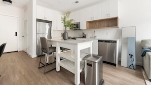 Una cocina moderna con armarios blancos, electrodomésticos de acero inoxidable y un estante de madera.