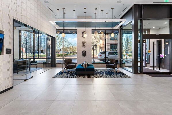 A modern lobby with a reception desk, seating area, and large windows offering views of the street. - Landing | Stylish 1BD, Courtyard, Gym (Alexandria)
