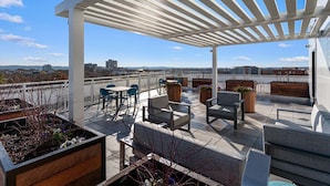 Eine Dachterrasse mit Sitzgelegenheiten im Freien, einer Pergola und Blick auf die Stadtlandschaft.