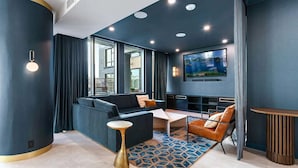 Ein modernes Wohnzimmer mit einem dunkelblauen Sofa, einem Ledersessel, einem Couchtisch und einem großen Flachbildfernseher an der Wand.