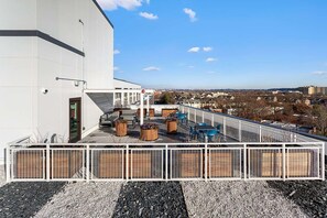 Una terraza en la azotea con mobiliario exterior, vistas a la ciudad y fachada de un edificio blanco.