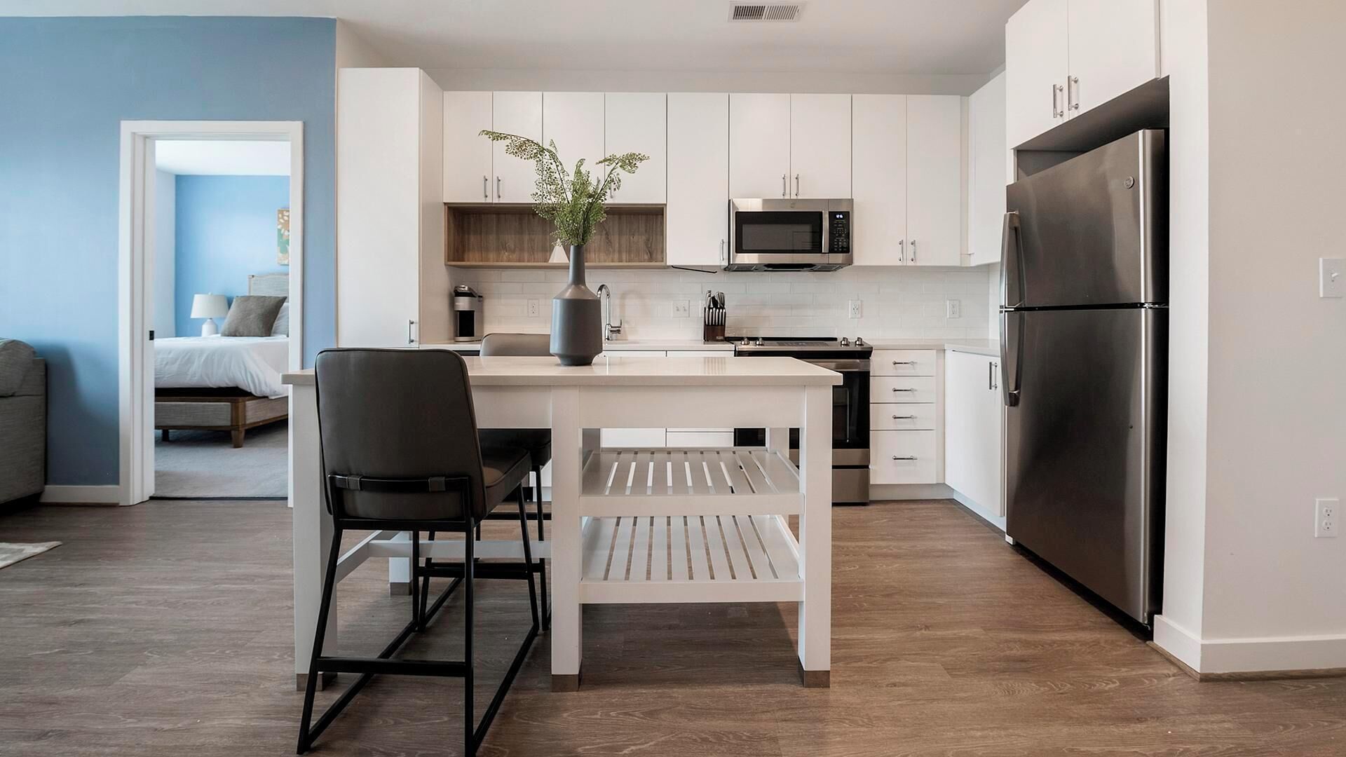 Een moderne keuken met witte kasten, een zwarte koelkast en een eethoek met een witte tafel en zwarte stoelen.