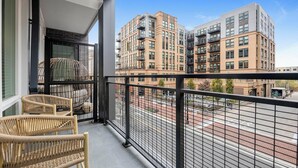 Een balkon met rieten stoelen, uitzicht op een stadsgezicht met moderne gebouwen en een heldere lucht.