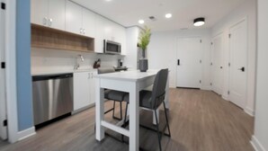 Een moderne keuken met witte kasten, een roestvrijstalen vaatwasser en een witte eettafel met twee stoelen.