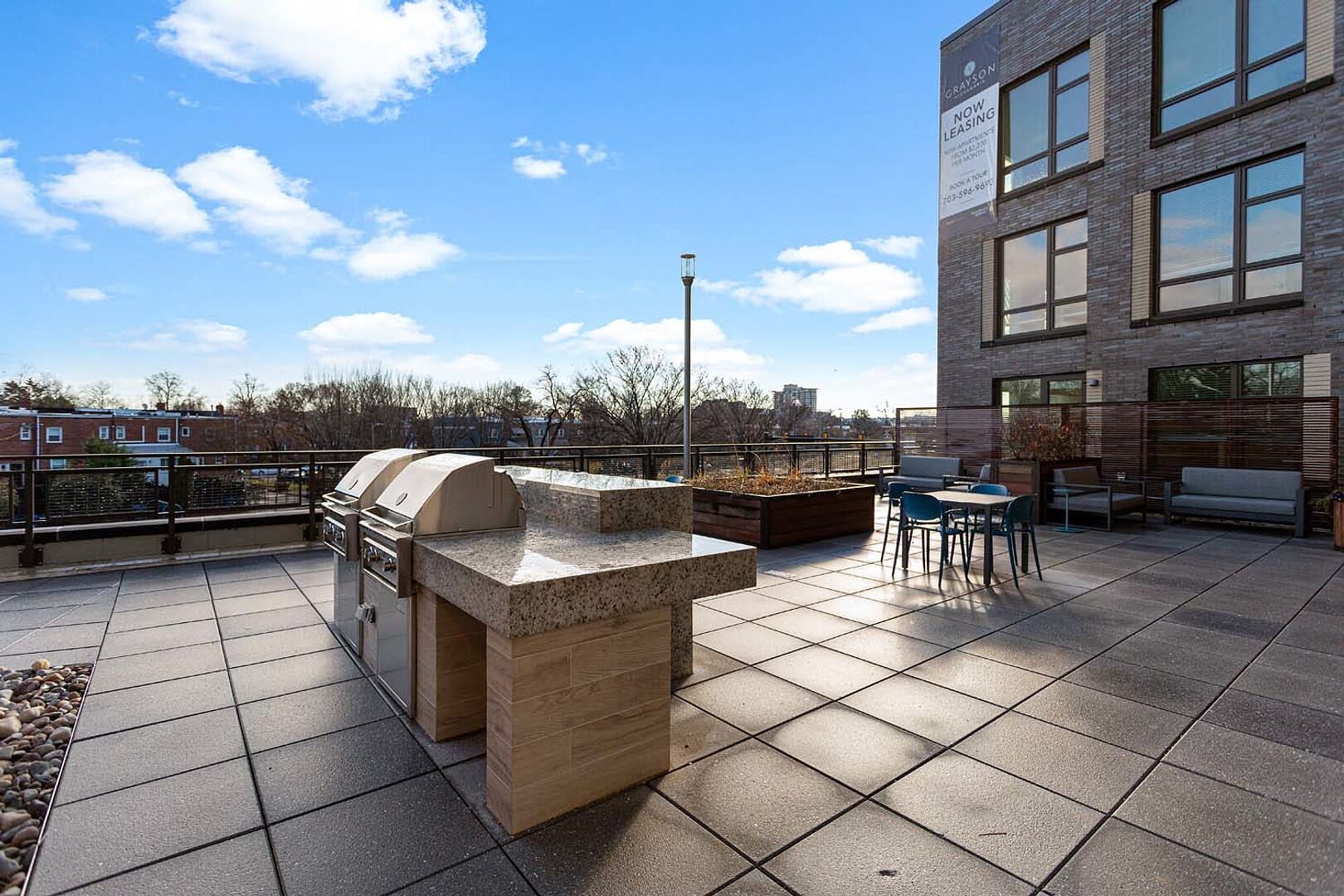 An outdoor patio with a barbecue grill, seating area, and a view of the cityscape.