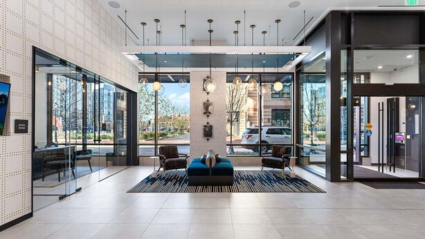 A modern lobby with a reception desk, seating area, and large windows offering views of the outside. - Landing | Amazing 2BD, Clubhouse, Courtyard (Alexandria)