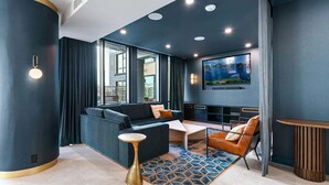 A modern living room with a dark blue sofa, a leather armchair, a coffee table, and a large flat-screen TV mounted on the wall. - Landing | Modern 2BD, Courtyard, Gym (Alexandria)