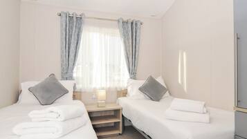 A hotel room with two single beds, a nightstand with a lamp, and a window with curtains.