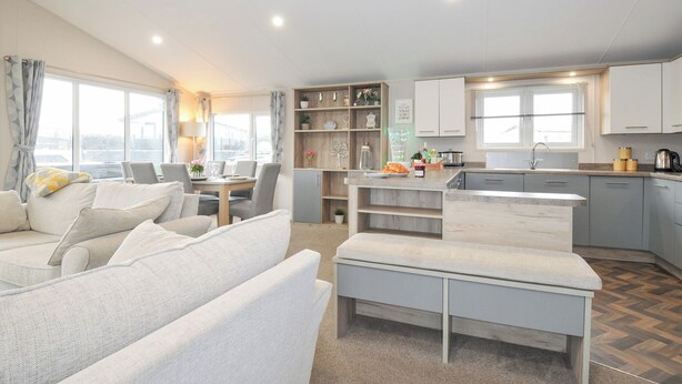 A modern living room with a sofa, a dining table, and a kitchen area with cabinets and a countertop. - 2 Summerleaze (Bude)