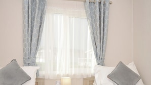 A hotel room with two beds, a bedside table with a lamp, and a window with patterned curtains. - 2 Summerleaze (Bude)