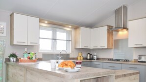 A modern kitchen with a central island, white cabinetry, stainless steel appliances, and a window with blinds. - 2 Summerleaze (Bude)
