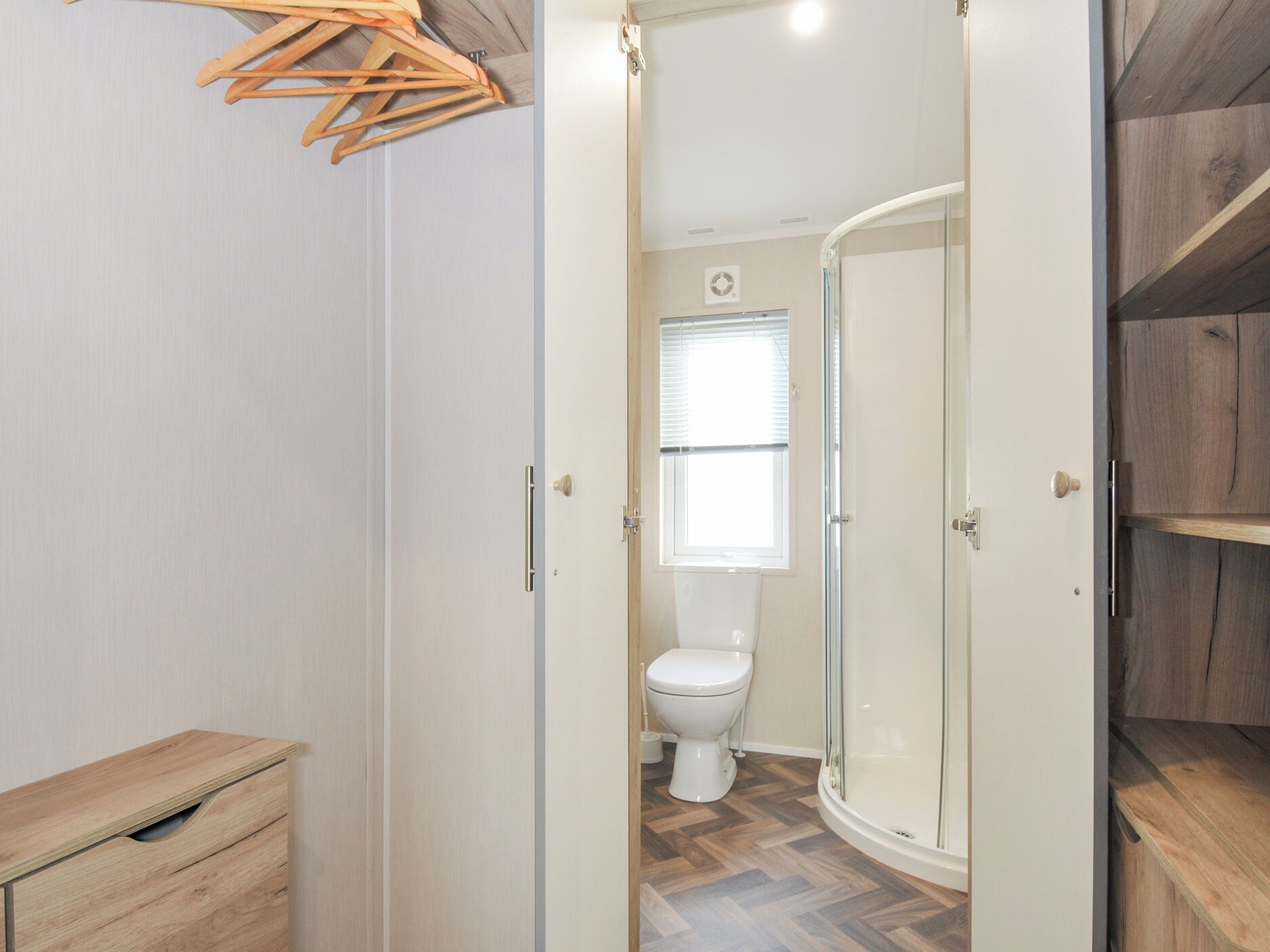 A bathroom with a toilet, a shower, and a wooden cabinet.
