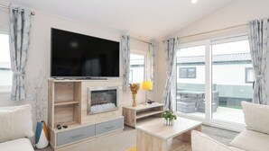A modern living room with a flat-screen TV, a fireplace, a sofa, and a dining area with a table and chairs. - 2 Summerleaze (Bude)