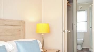 A bedroom with a bed, a nightstand, a lamp, and a door leading to a bathroom.