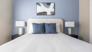 Un lit bien fait, avec du linge de lit blanc, deux oreillers et deux tables de chevet dotées de lampes.