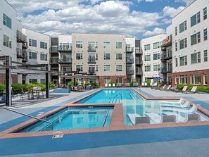 Un immeuble d’appartements moderne doté d’une piscine centrale, d’un espace extérieur aménagé et d’un patio couvert.