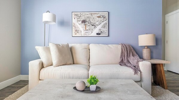Un salon avec un mur bleu clair, un canapé blanc agrémenté de coussins, une table basse ornée d’objets décoratifs, un lampadaire et une table d’appoint avec une lampe.