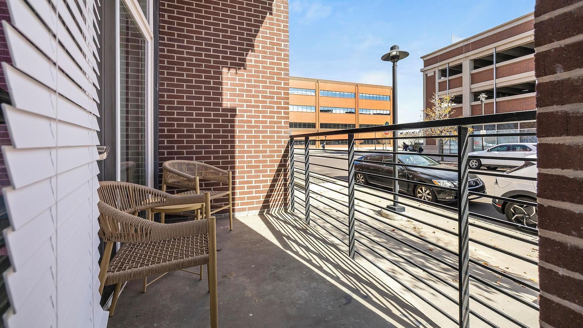 A balcony with wicker chairs, a metal railing, and a view of a parking garage.