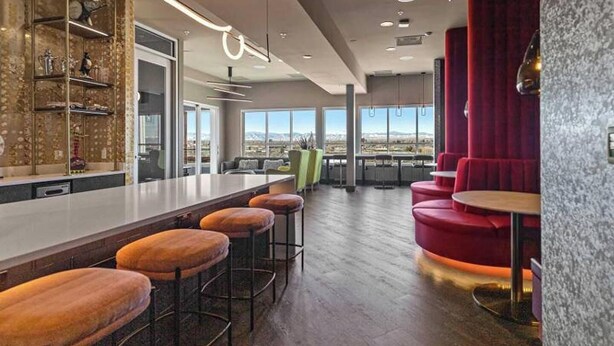 Eine moderne Bar mit einer langen Theke, mehreren Hockstühlen und Blick auf die Stadt durch große Fenster.