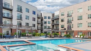 Ein modernes Apartmenthaus mit einem zentralen Schwimmbad, Sitzgelegenheiten im Freien und einer überdachten Terrasse.
