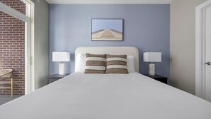A neatly made bed with white bedding and striped pillows, flanked by two bedside tables with lamps, against a blue wall with a framed picture above. - Landing | Modern 2BD, Gym, Clubhouse (Denver)