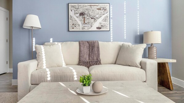 A living room with a sofa, a coffee table with a plant and a vase, a lamp, and a framed artwork on the wall. - Landing | Modern 2BD, Gym, Clubhouse (Denver)