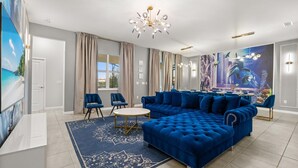 Ein modernes Wohnzimmer mit einem blauen Ecksofa, zwei Sesseln, einem runden Couchtisch und einer Pendelleuchte.