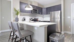 A modern kitchen with dark cabinets, a stainless steel refrigerator, a built-in oven, and a bar area with two bar stools. - Landing | Modern 2BD, Gym, Clubhouse (Denver)