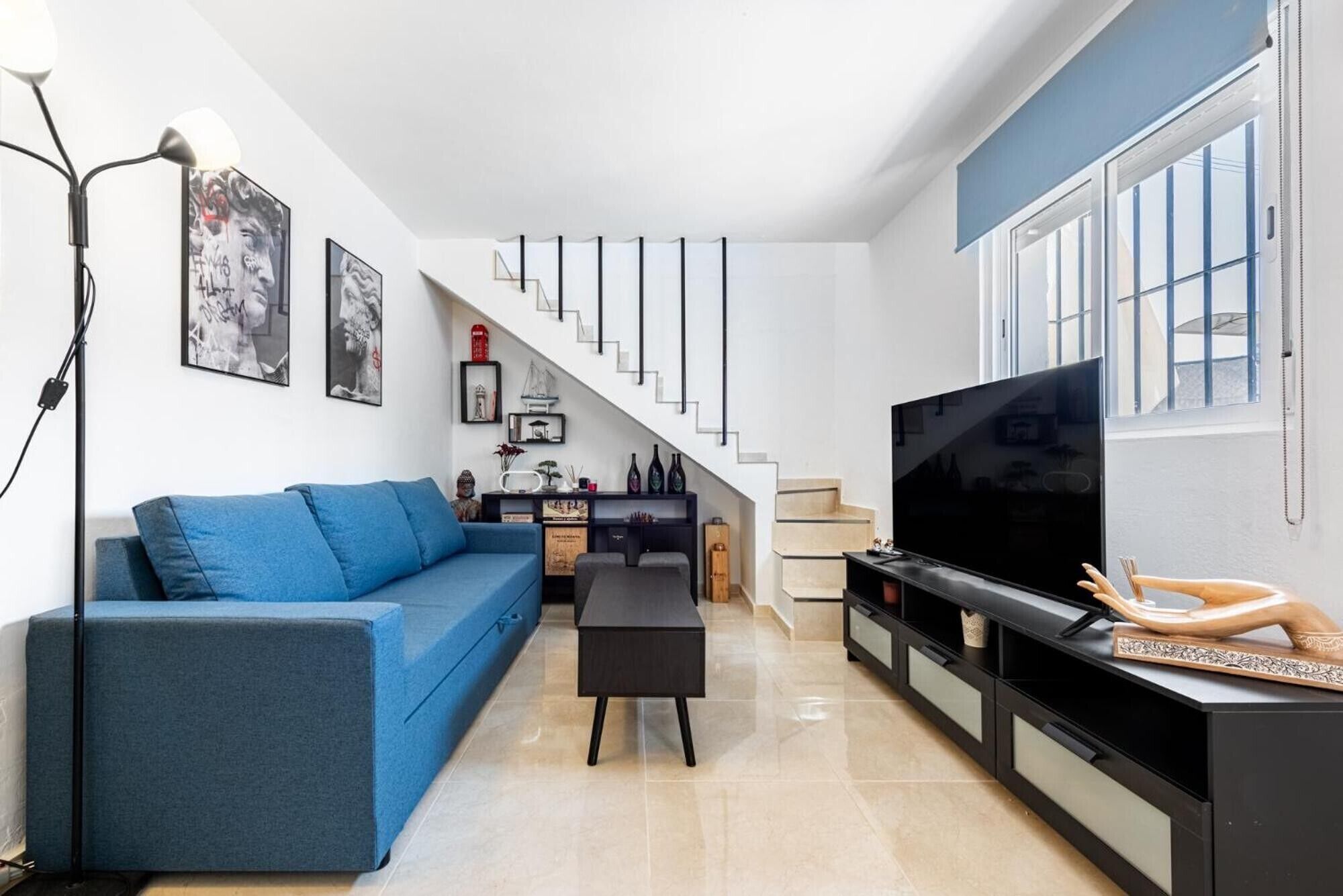 A modern living room with a blue sofa, a black coffee table, a TV, and a staircase leading to another level.