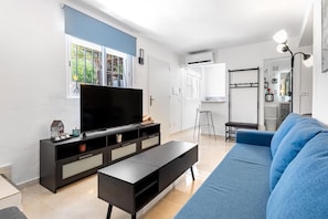 Ein modernes Wohnzimmer mit einem Flachbildfernseher, einem blauen Sofa, einer schwarzen Unterhaltungsecke und einer Küche im Hintergrund.