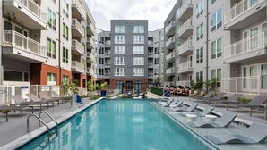 En moderne lejlighedsejendom med en central pool, flere balkoner og liggestole omkring poolen.