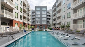 Un immeuble d’appartements moderne doté d’une piscine centrale, de nombreux balcons et de chaises longues disposées autour de la piscine.