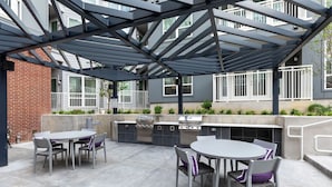 Une terrasse extérieure dotée d’un barbecue et d’un espace salon, le tout entouré d’une structure de pergola en métal.