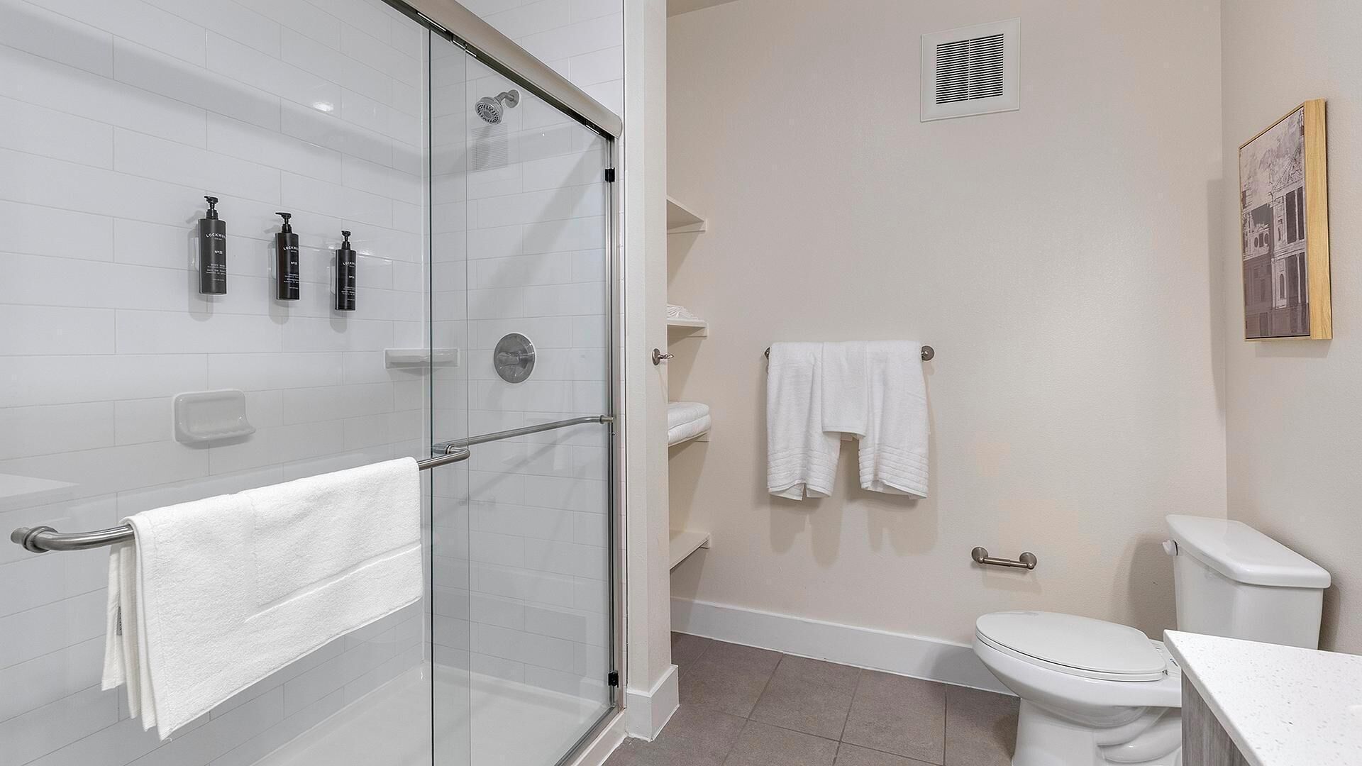 Een moderne badkamer met een douchecabine van glas, witte tegels, een toilet en een wastafel.