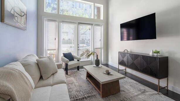 Un salon moderne comprenant un canapé, un fauteuil, une table basse et un téléviseur fixé au mur.
