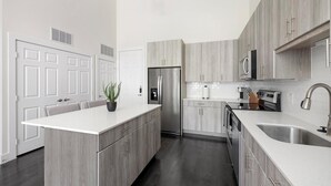 Une cuisine moderne avec des meubles de couleur grise, un réfrigérateur en acier inoxydable, un four à micro-ondes et un évier.
