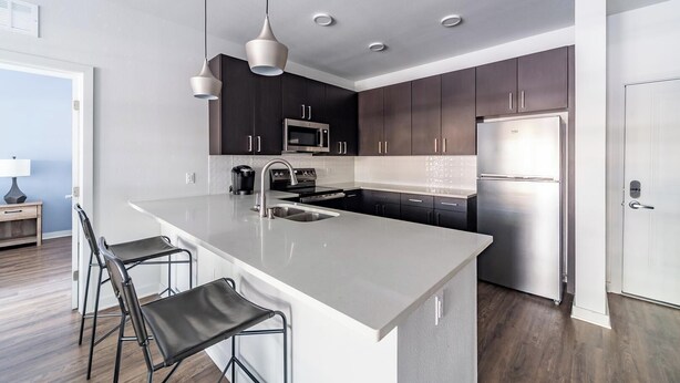 Una cocina moderna con gabinetes oscuros, electrodomésticos de acero inoxidable y una isla central con taburetes de bar.