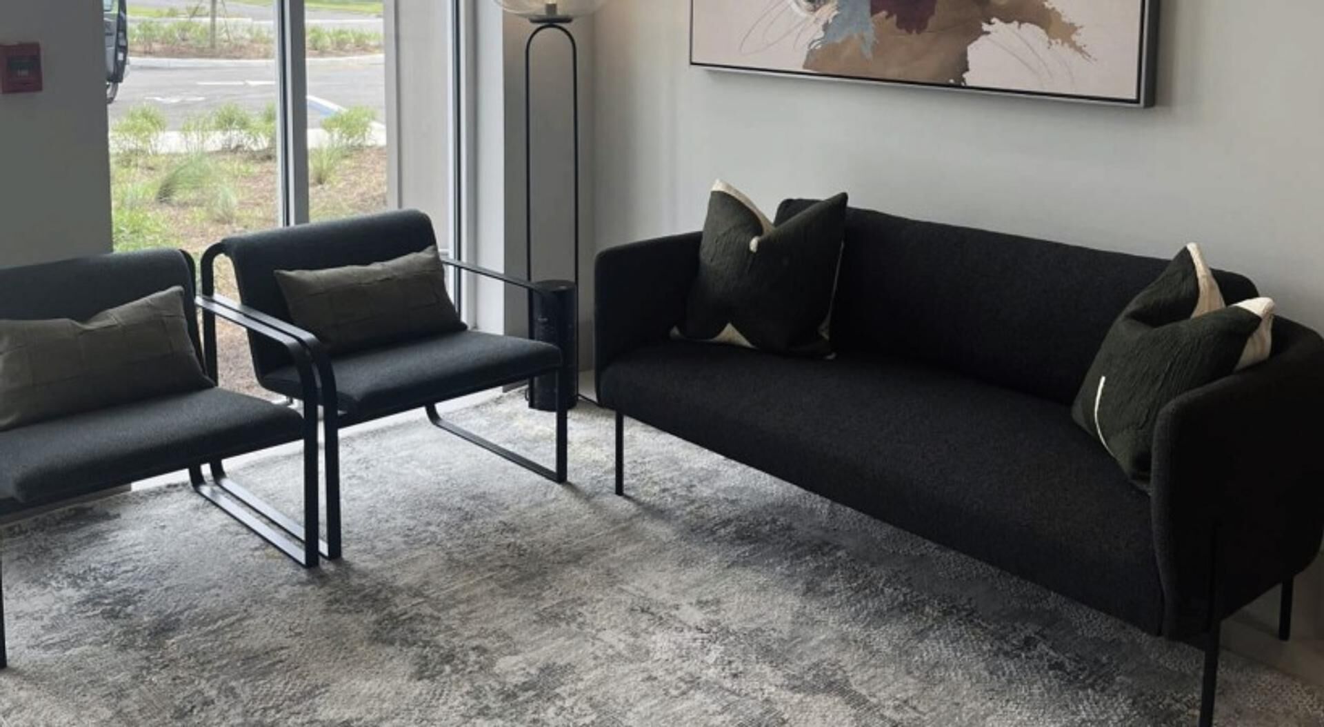 Un espace d’attente moderne avec un canapé noir, un fauteuil noir et un tapis gris.