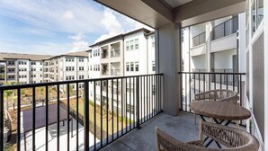 Ein Balkon mit Blick auf einen Wohnkomplex, eine gepflasterte Fläche und einen kleinen Garten.