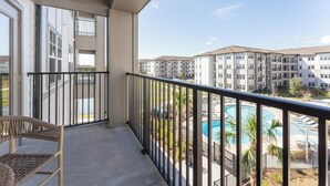 Ein Balkon mit Korbstuhl, Blick auf einen Swimmingpool und angrenzende Wohnhäuser.