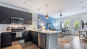 Una cocina moderna con armarios oscuros, electrodomésticos de acero inoxidable, una isla central, iluminación colgante y vistas a un balcón.