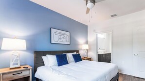Une chambre d’hôtel moderne avec un grand lit, deux tables de chevet avec des lampes, un ventilateur de plafond, une salle de bain avec un miroir et une porte.
