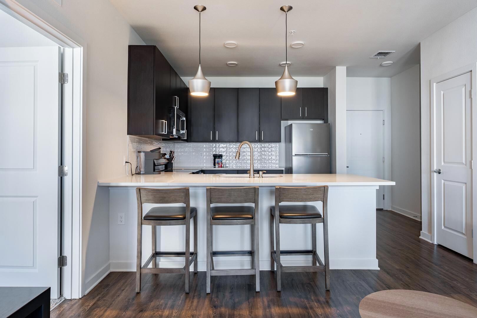 A modern kitchen with dark cabinets, a large island with bar stools, stainless steel appliances, and pendant lighting.
