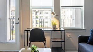 Een modern appartement met een bureau, stoel en uitzicht op een gebouw door grote ramen.