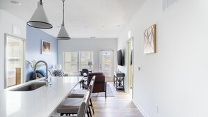 Una cocina moderna con una isla central, luces colgantes y un comedor con sillas.