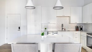A modern kitchen with white cabinetry, a large island with bar stools, stainless steel appliances, and pendant lighting. - Landing | Amazing 1BD, Gym, Pool (Orange Beach)
