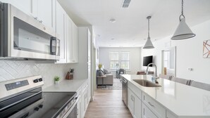 A modern kitchen with white cabinetry, stainless steel appliances, and a large island with a sink. - Landing | Stylish 2BD, Gym, Yoga Studio (Orange Beach)