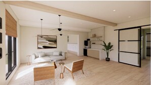 A modern living room with a white sofa, wooden coffee table, and a dining area with a white table and chairs. There is a large window with blinds, a hanging light fixture, and a potted plant. - Landing | Stylish 2BD, Gym, Yoga Studio (Orange Beach)