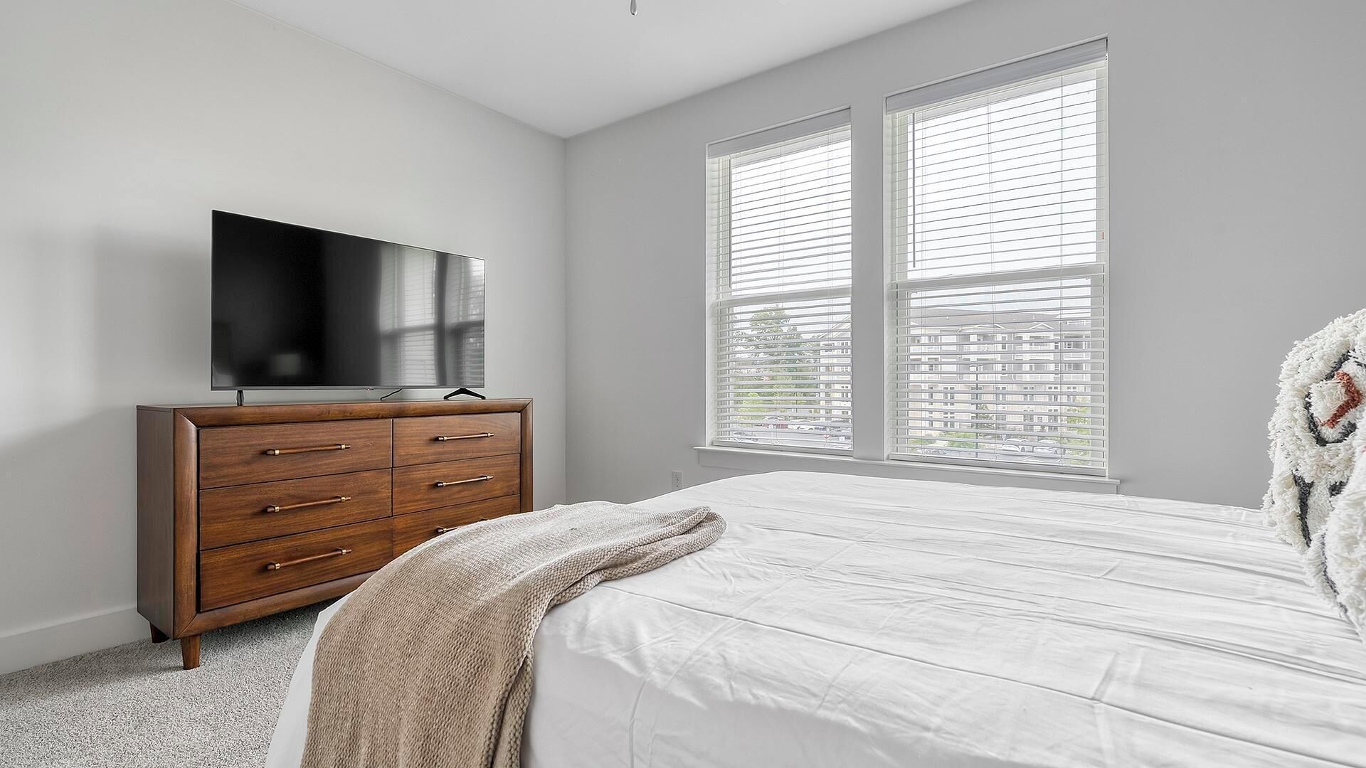 Un dormitorio con una cama grande, un aparador de madera, un televisor de pantalla plana y una ventana con persianas.
