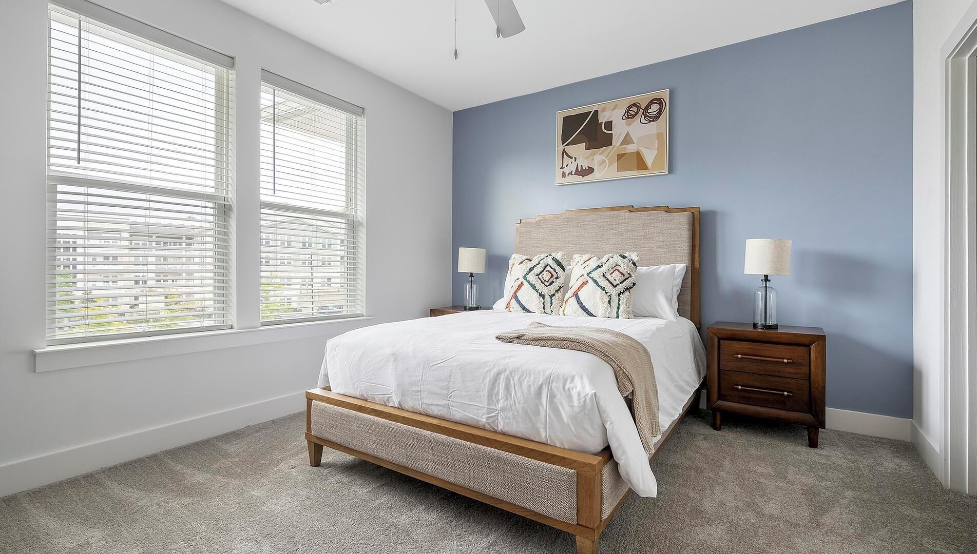 A bedroom with a bed, two bedside tables, a ceiling fan, and a window with blinds.